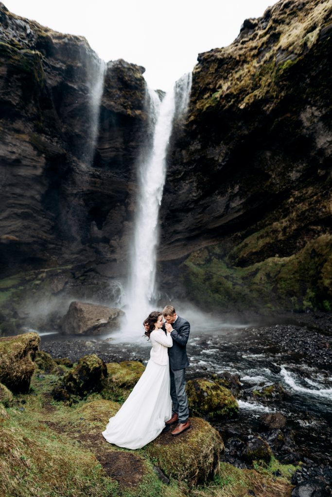 wedding couple standing in front of cascading waterfall Iceland wedding