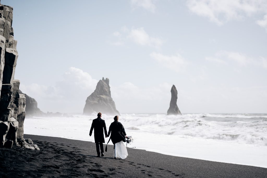 wedding couple strolling along black sand beach Iceland wedding