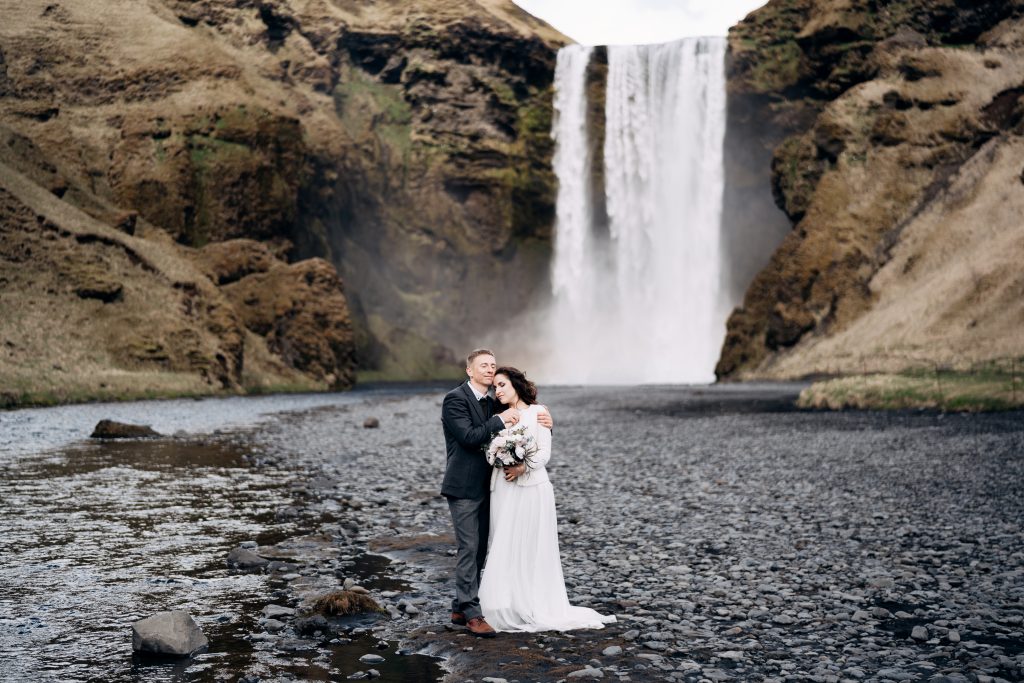 couple in wedding attire in front of powerful waterfall Iceland wedding