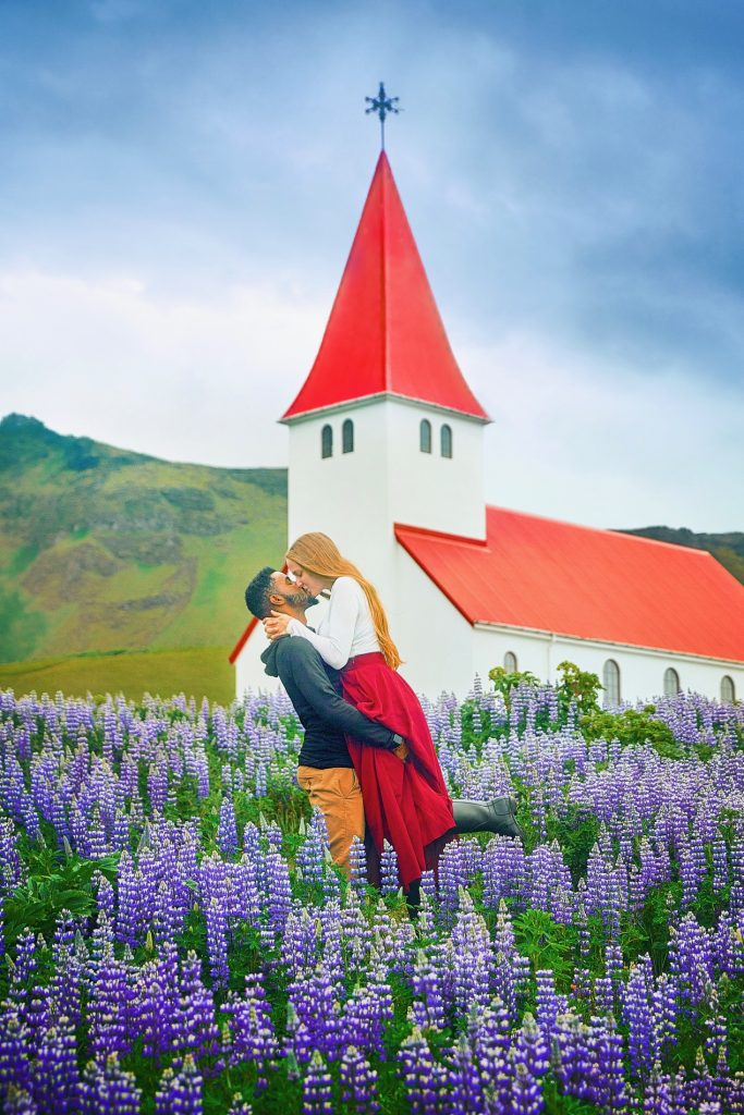 couple kissing in field of purple flowers in front of red roofed church Iceland wedding