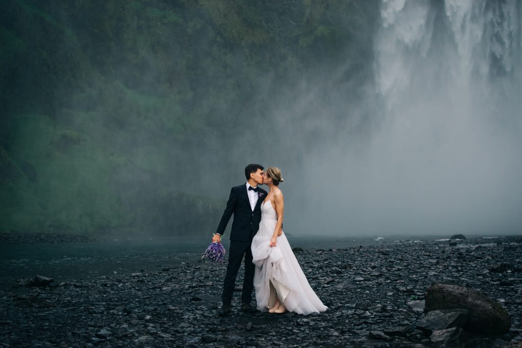 newly married couple kissing in front of Iceland waterfall