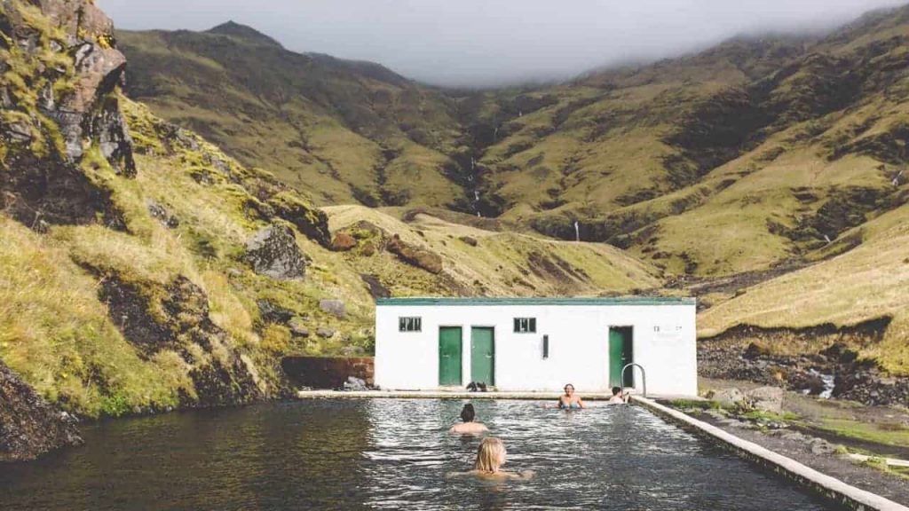 hot spring in the middle of iceland with green grass and waterfalls in the background