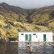 people swimming in a remote swimming pool in iceland with green mountains and fog in the background