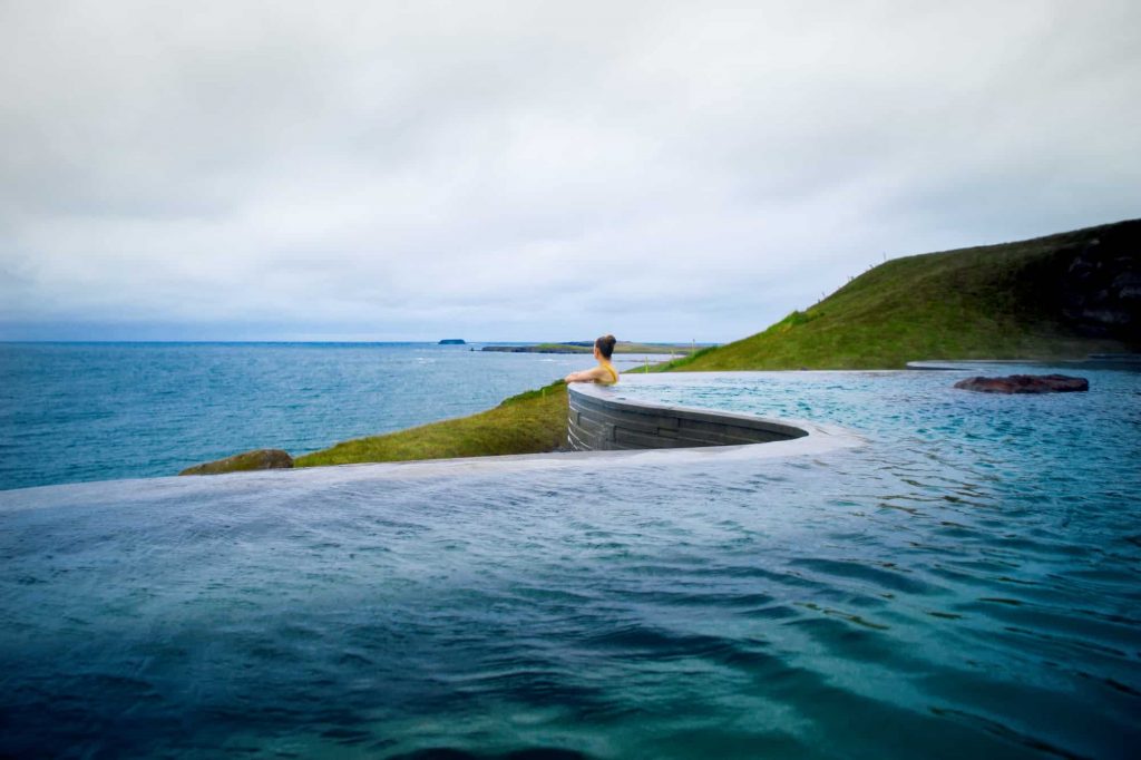 Woman leaning over the edge of a geothermal pool in Iceland overlooking the ocean.