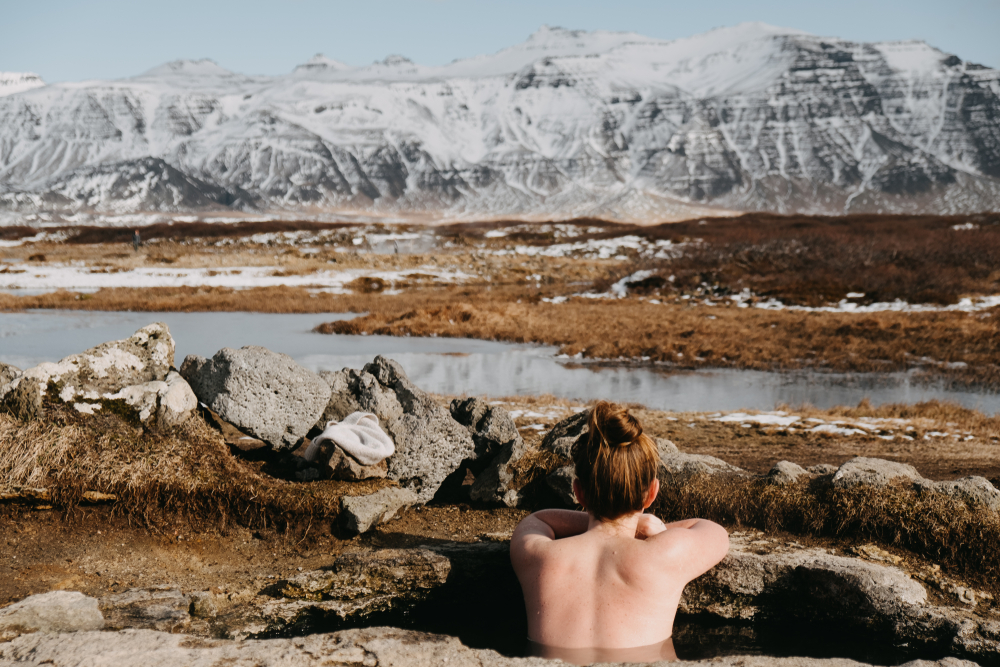 Woman sitting in Landbrotalaug Hot Springs in Iceland, staring at distance snowy mountains.