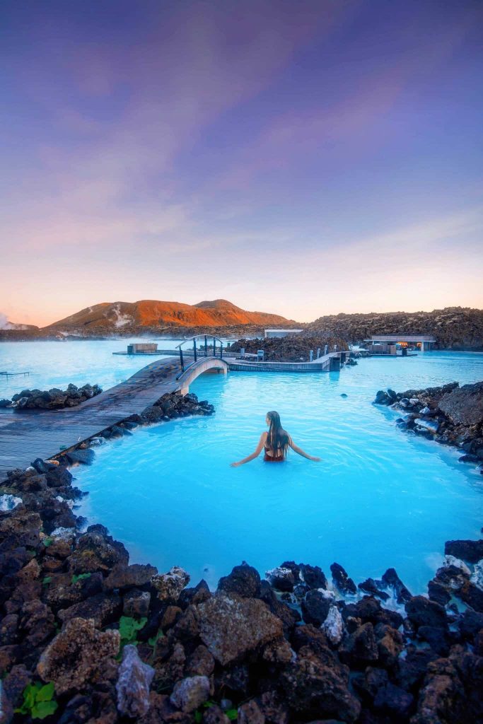 Woman standing in the blue waters of the Blue  Lagoon at dusk, one of the best hot springs in Iceland.