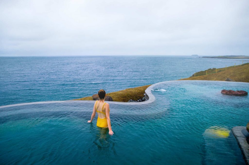 Woman standing in yellow bathing suit in a pool at Geosea Sea Baths overlooking the ocean.