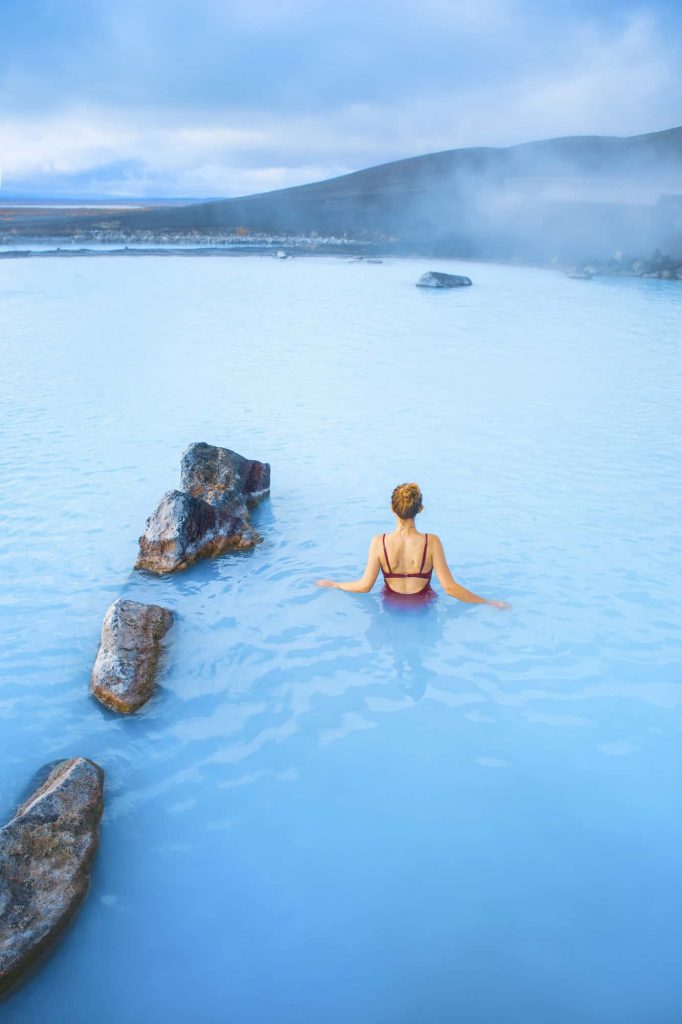 Woman standing in milky blue water next to rocks in the Mývatn Nature Baths.