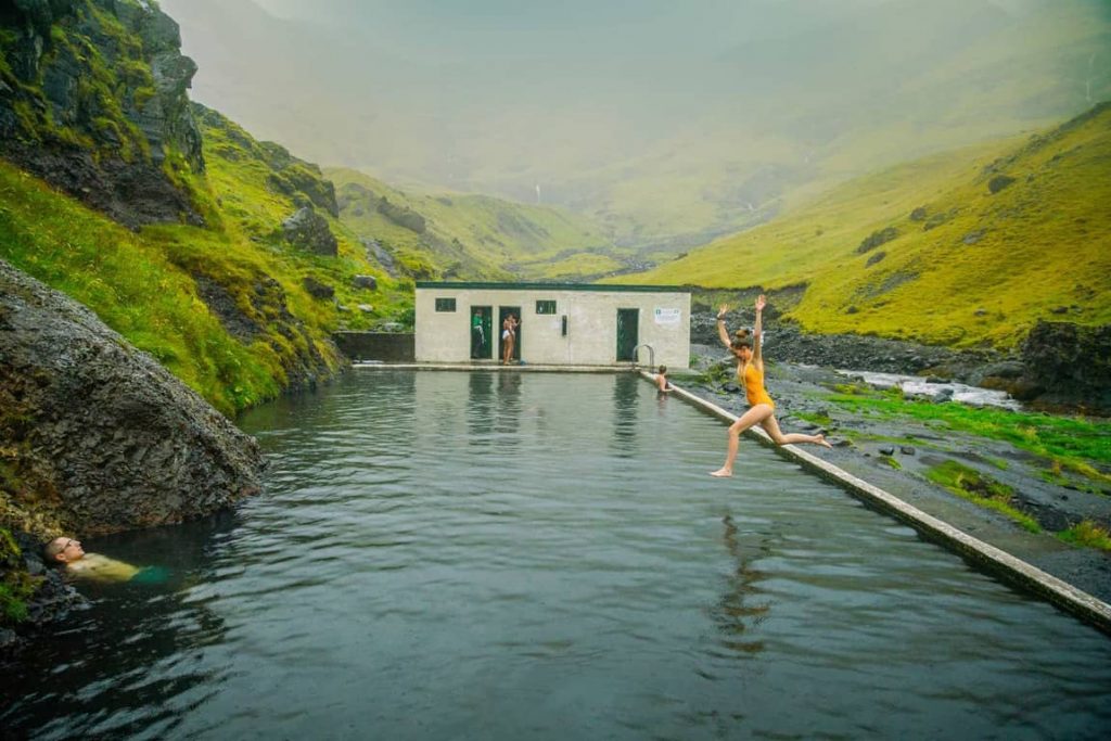 woman in yellow bathing suit jumping into a pool called seljavallalaug hot springs in iceland