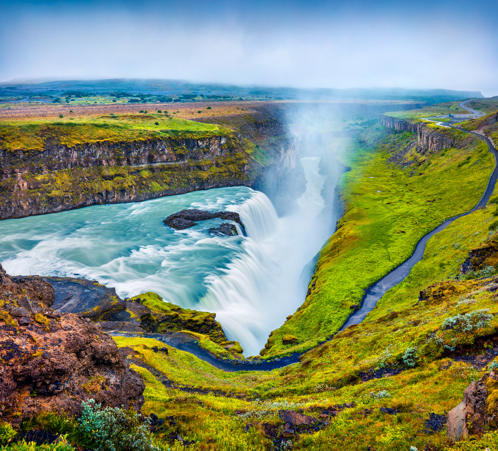 Iceland's gullfoss waterfall plunging into canyon on a cloudy day with green grass