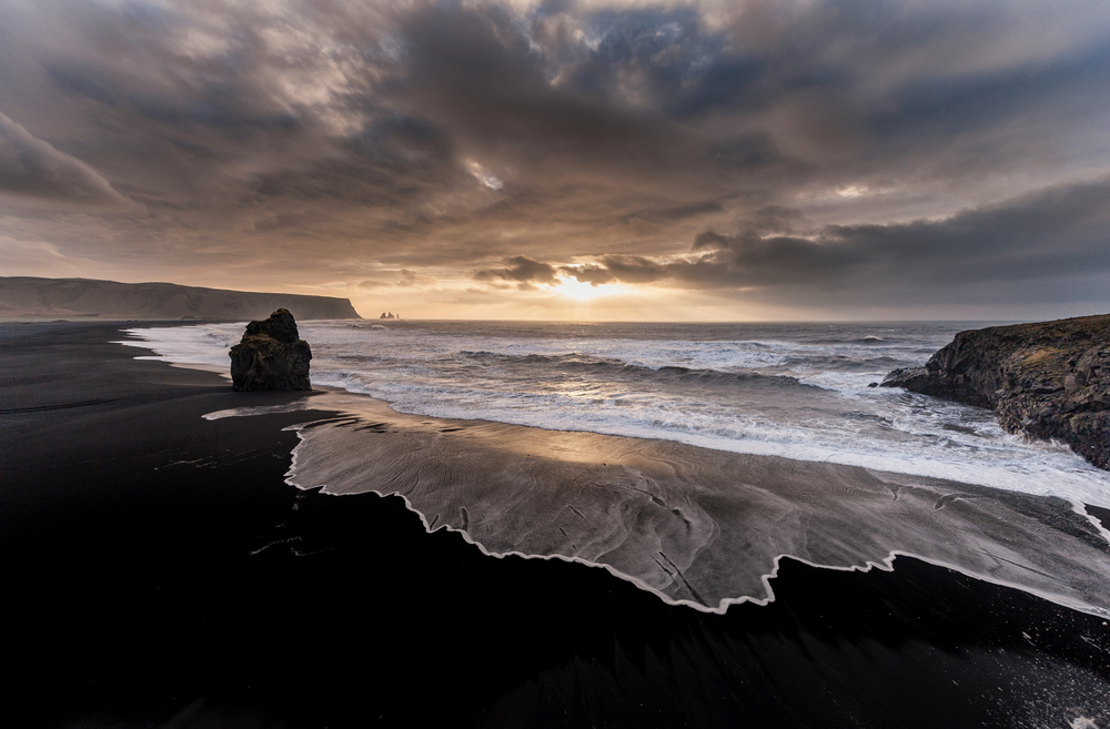 black sand beach in iceland with waves on it at sunset