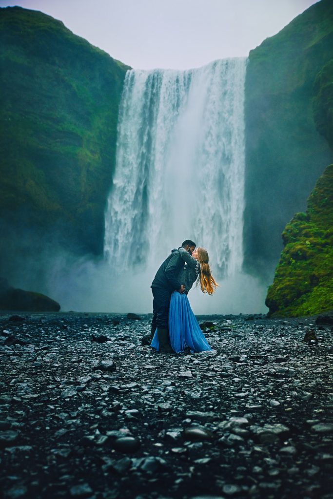 a couple kissing in front of skogafoss waterfall in iceland on a cloudy moody day