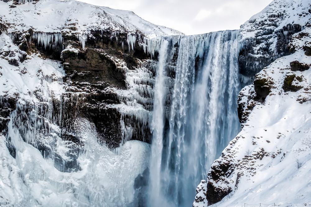 close up of skogafoss waterfall in iceland surrounded by snow on a cloudy winter day