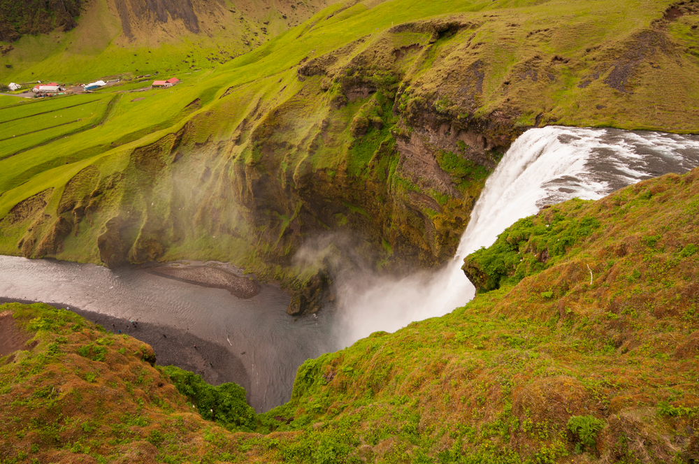 a view from the top of skogafoss waterfall in iceland surrounded by green grass on a nice summer day