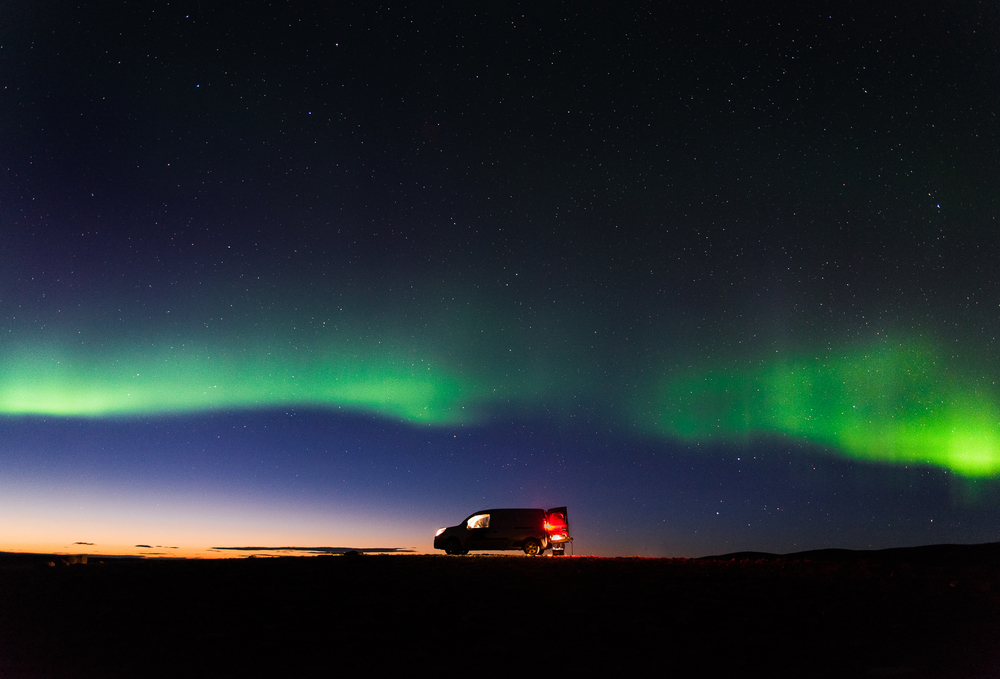 The Northern Lights shining above a campervan in Iceland.