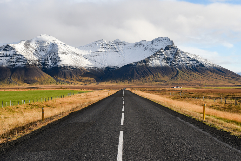 A black, paved road stretching towards snowy mountains.