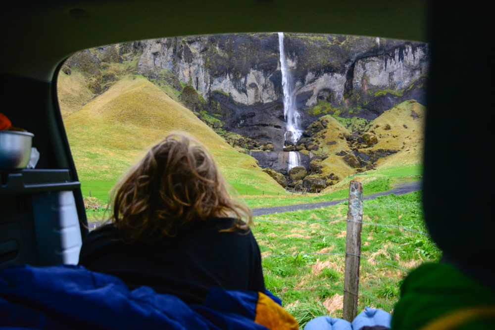 A women sitting in the back of a campervan in Iceland, looking out at a waterfall.