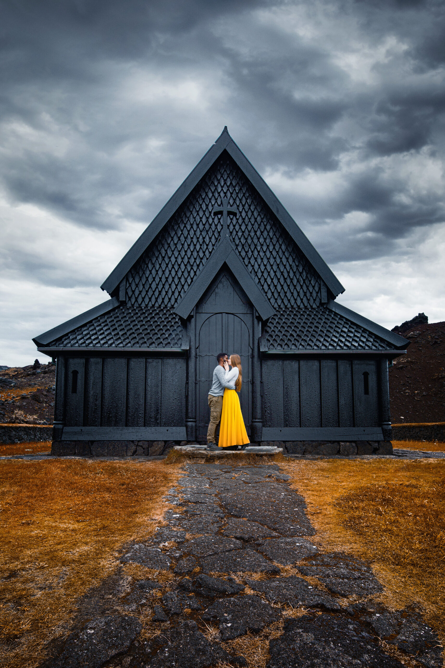 Couple standing and kissing in front of Heimaey Stave Church in Iceland on a moody day