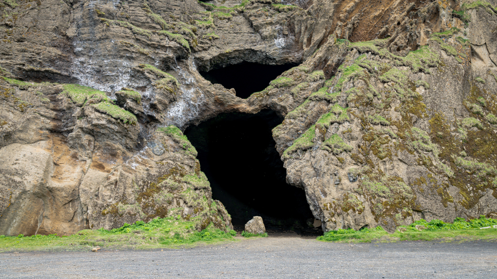 Cave opening on black sand beach with green moss around it