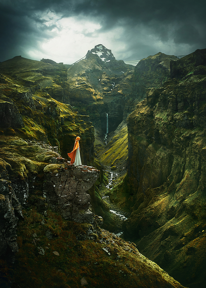 Woman in yellow cape standing in a cliff at Mulagljufur Canyon one of the best hidden gems in iceland