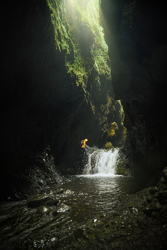 Woman in yellow jacket hiking near waterfall in ravine in Iceland with Nauthusagil Waterfall in background