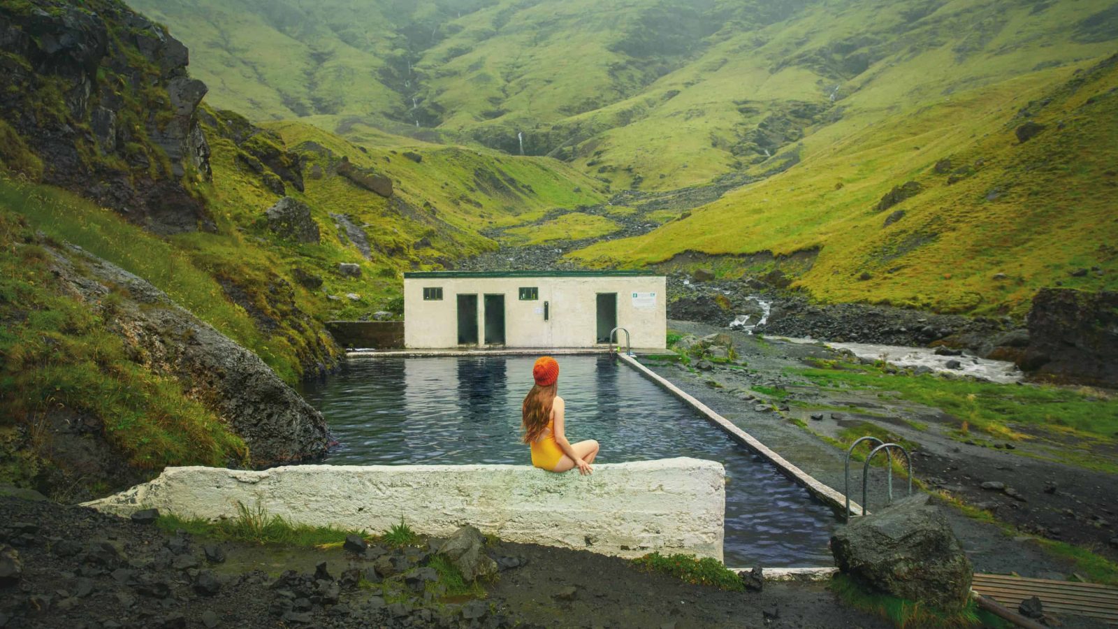 woman in yellow bathing suit sitting on the edge of Seljavallalaug Pool in Iceland