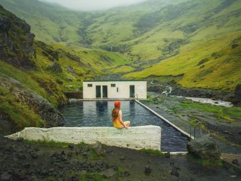 woman in yellow bathing suit sitting on the edge of Seljavallalaug Pool in Iceland