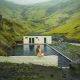 woman in yellow bathing suit sitting on the edge of Seljavallalaug Pool in Iceland
