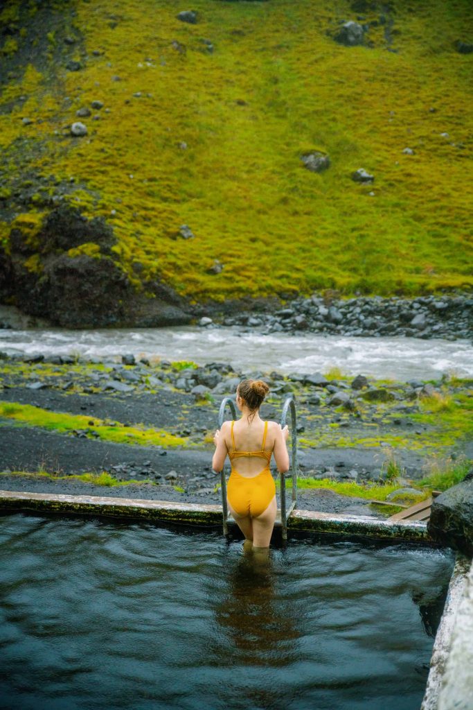 woman on a ladder climbing out of Seljavallalaug pool wearing a yellow bathing suit