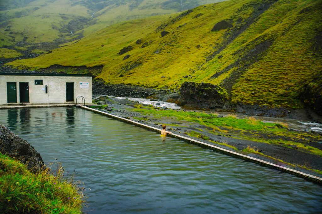 Woman in the water resting on the side of Seljavallalaug pool wearing a yellow swimsuit