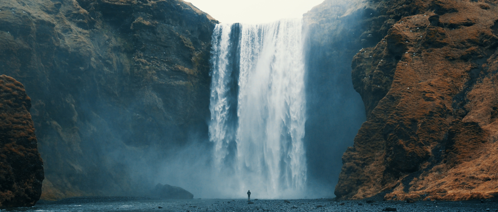 person standing infront of skogafoss waterfall in iceland on a moody day