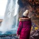 woman wearing a purple coat showing off one of the best jackets for iceland in front of a waterfall