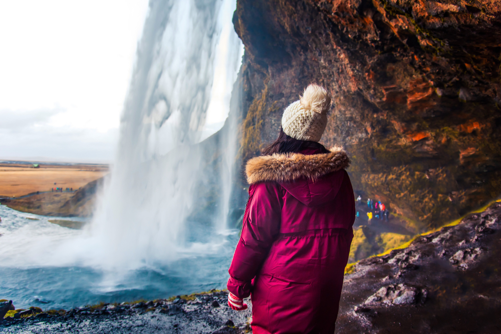 Woman standing looking at a waterfall wearing a purple winter jacket