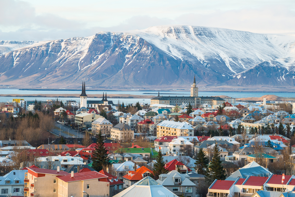 a picture of Reykjavik with various colored buildings and a distant snow covered mountain across the river