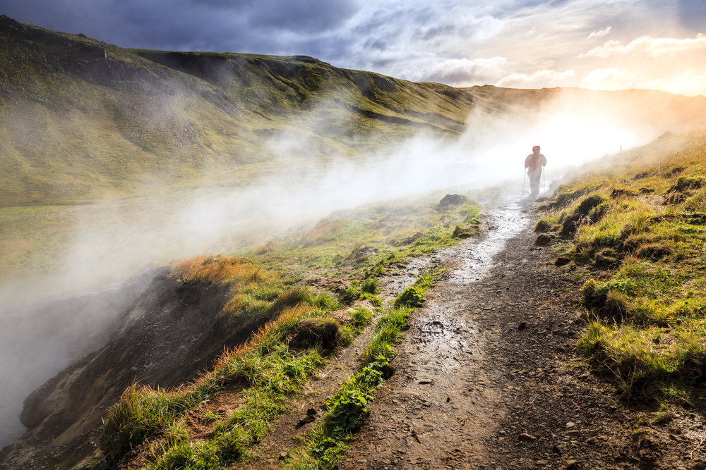 person shrouded in mist hiking in Iceland upriver at a hot spring