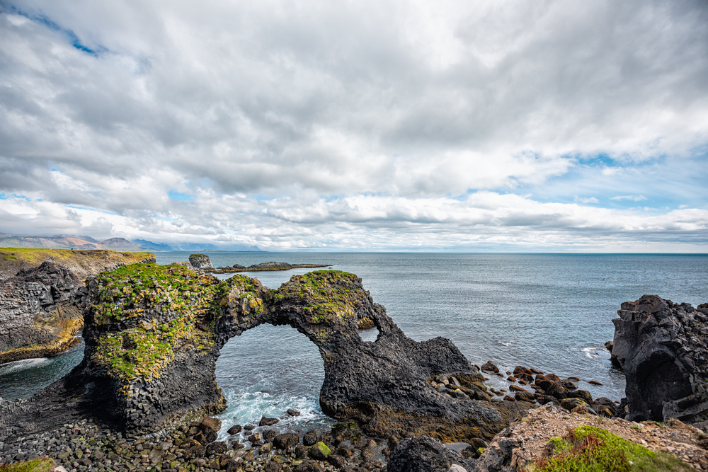 rock formations on the coast of iceland, one rock is in the shape of an arch. its a nice sunny day