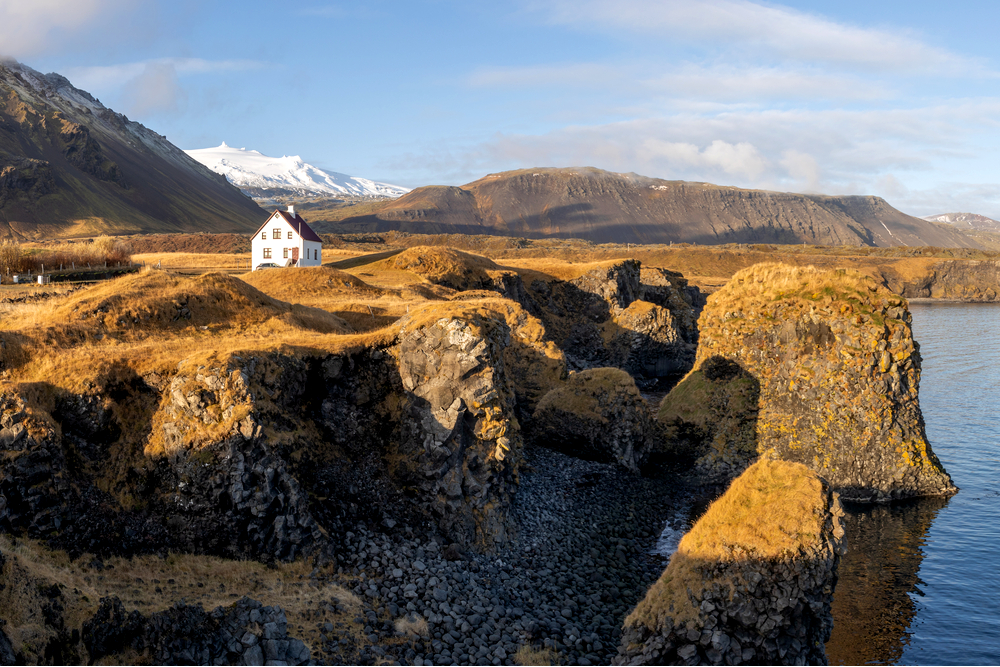 a white house with a red roof on the coast of iceland at sunset
