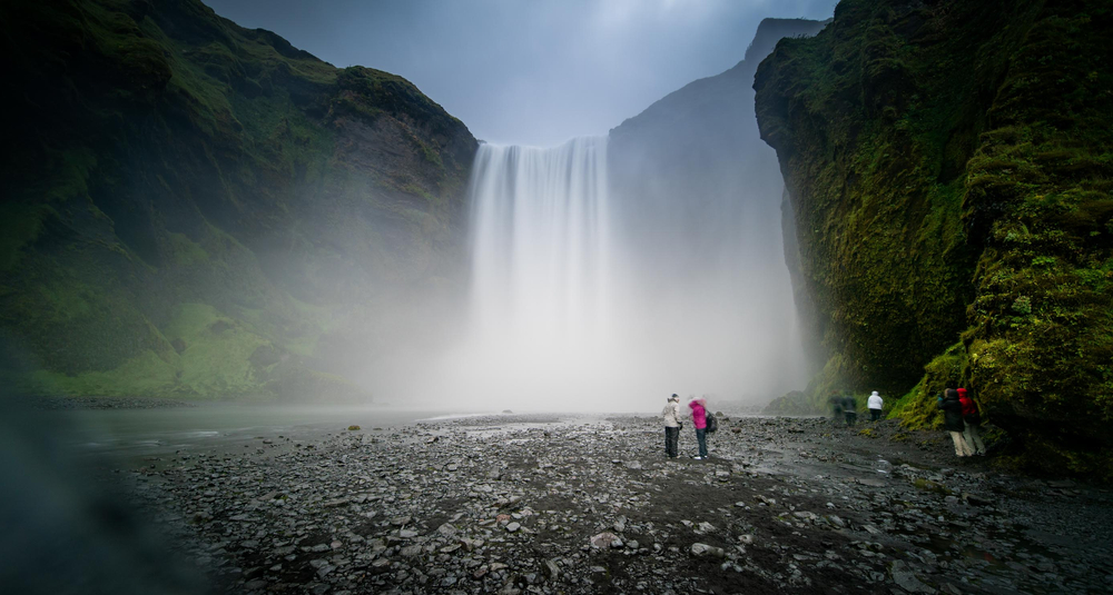 people hiking towards a large misty waterfall