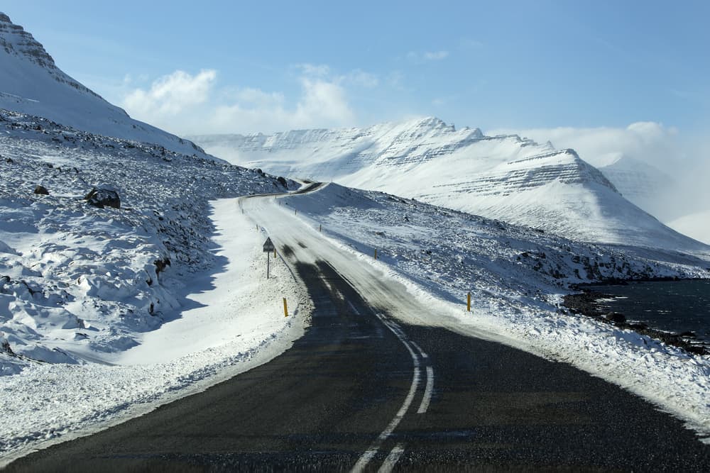 partially cleared road from snow on a sunny winter day with snow covered mountains in the distance in Iceland in November