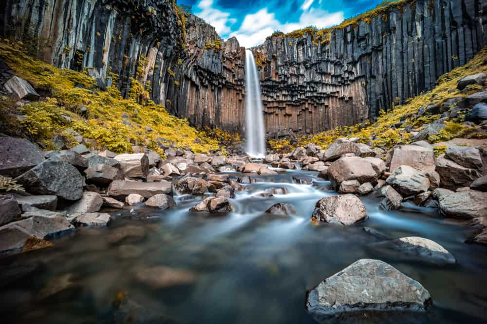 waterfall surrounded by basalt columns on a sunny day with a river flowing