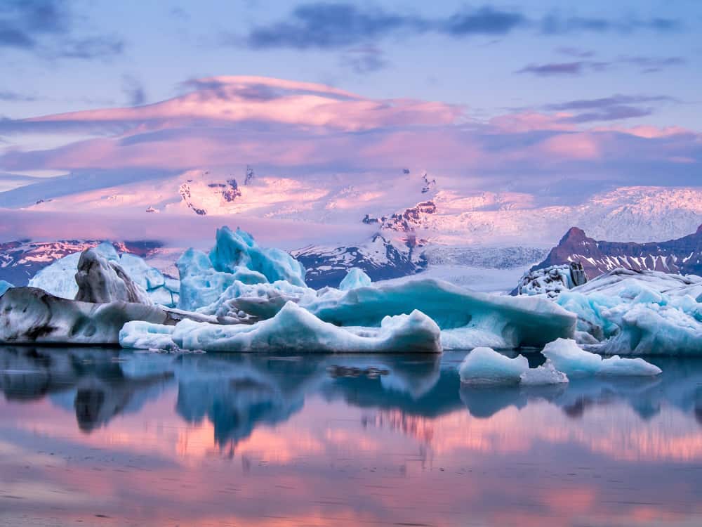 Glacier Lagoon with large icebergs and distant snow capped mountains at sunset in Iceland in December