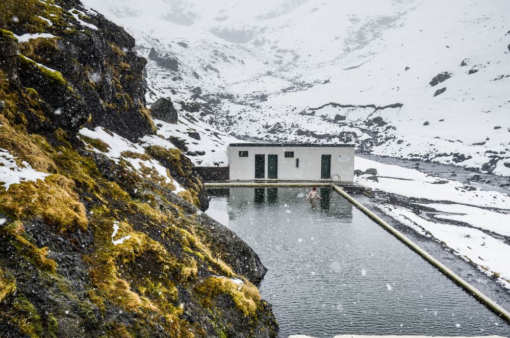 a man waist deep in a hot spring pool on a snowy moody day.