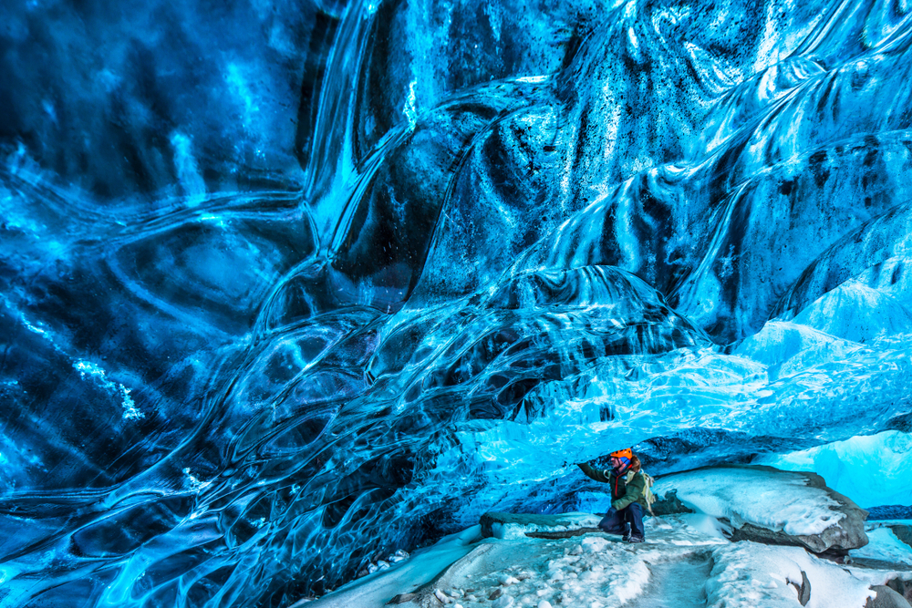  man in helmet in an ice cave with large blue ice wall above him during march in iceland