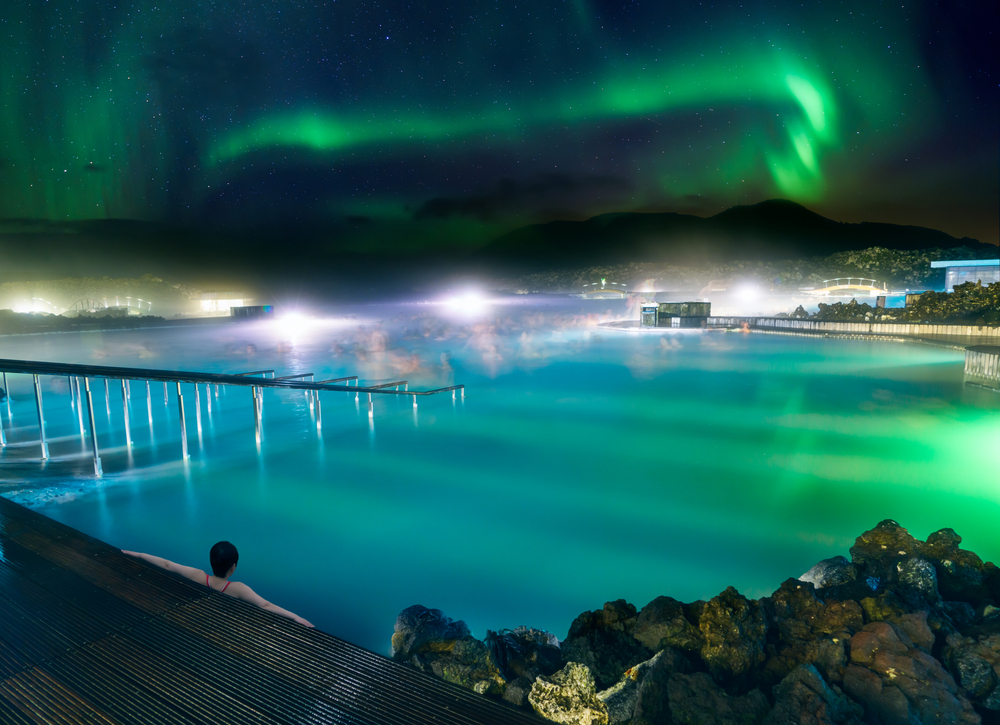 a tourist relaxing in the waters of the Blue Lagoon with the Northern Lights overhead