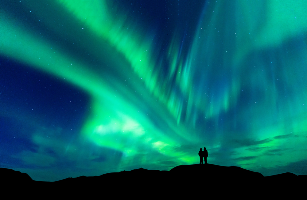 two tourists watching the Northern Lights from a hill