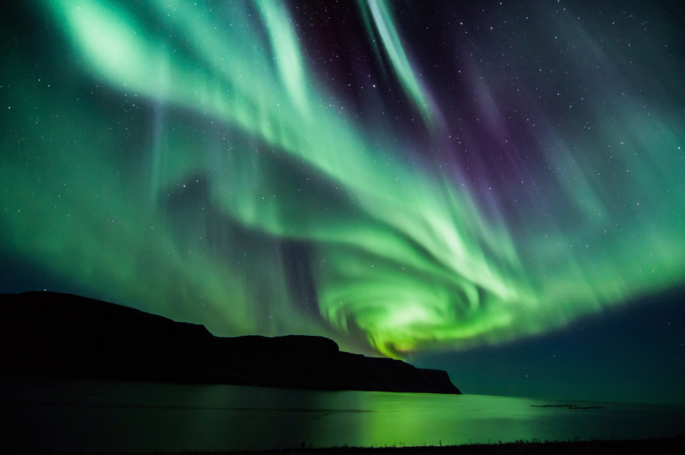 the Northern Lights swirling over mountains and a lake