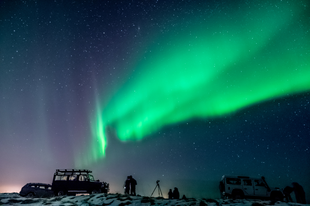 groups of tourists standing outside of their cars while watching the Northern Lights