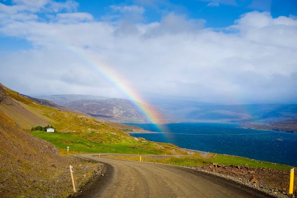 dirt road in the westfjords of Iceland on a sunny day with a rainbow above