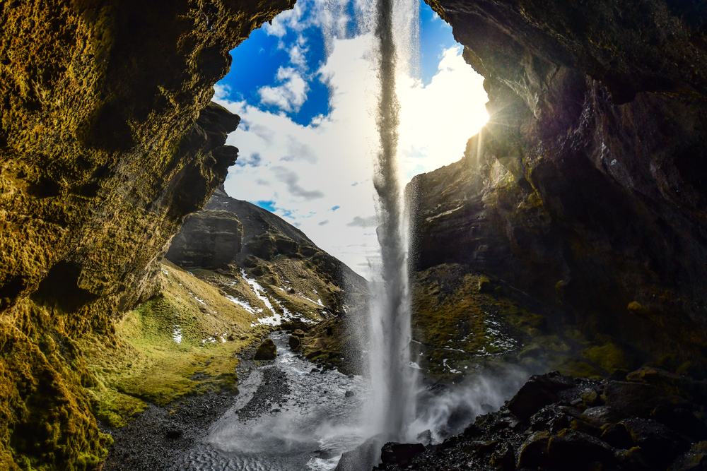 inside of Kvernufoss Canyon with a skinny waterfall flowing on a sunny day