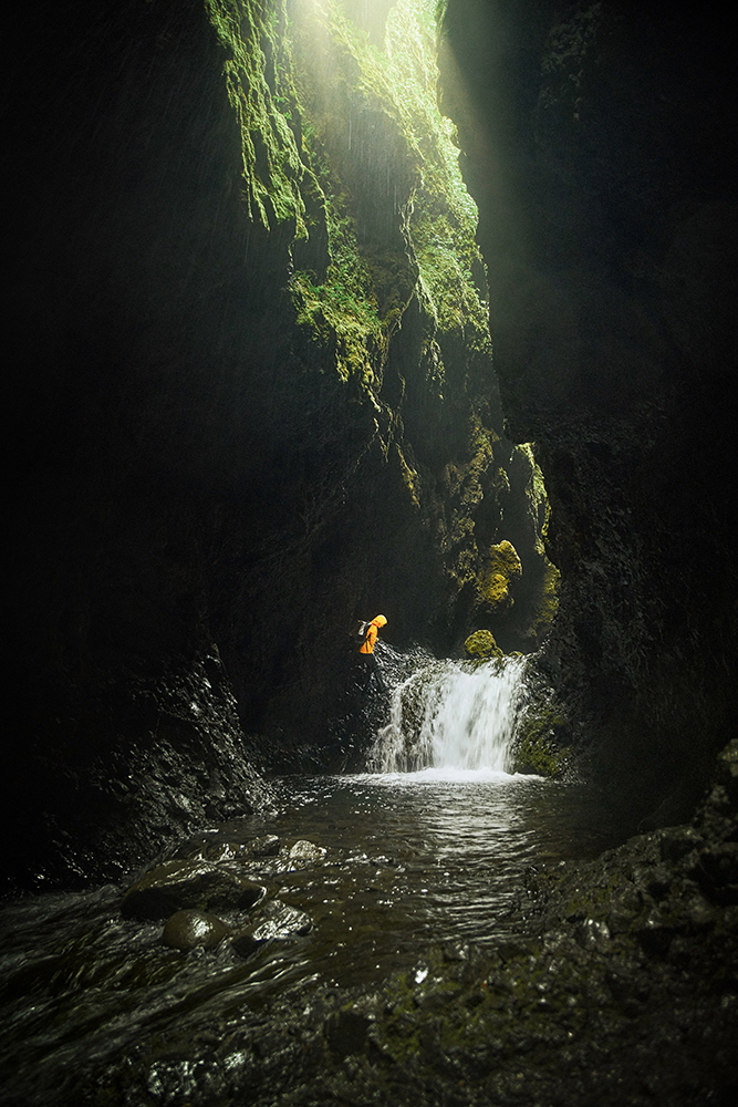 Nauthusagil Canyon in iceland with hiker climbing the side of a small waterfall surrounded by high moss covered canyon walls